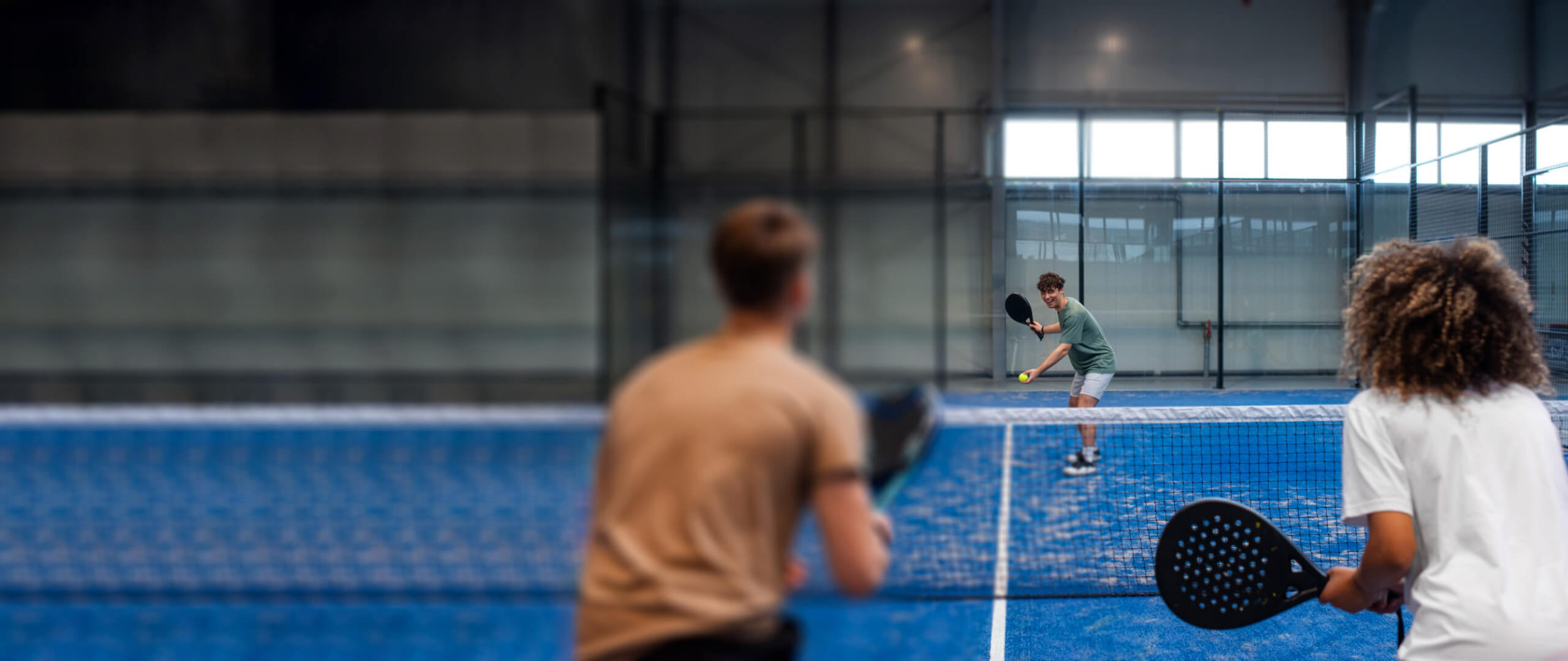 A group of people playing padel tennis in a modern indoor court at Padel Montreal.