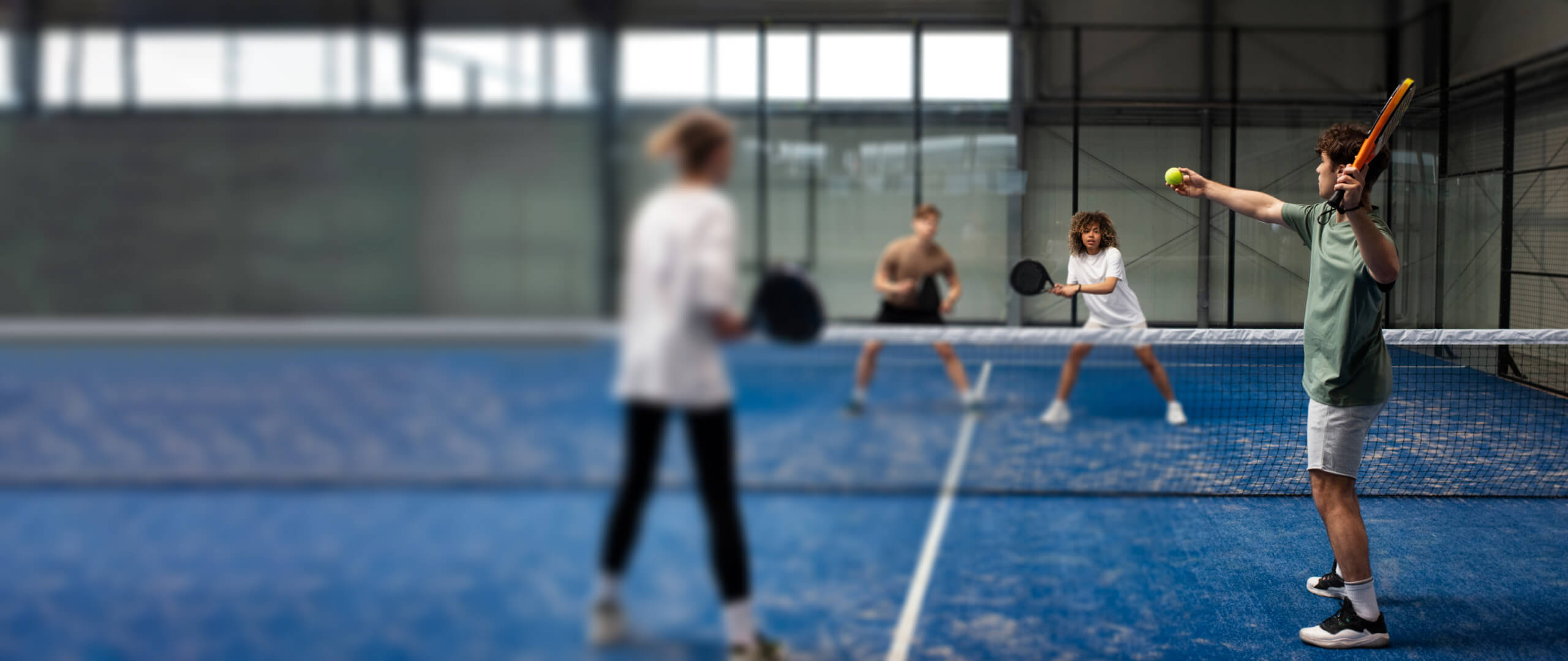 Padel tennis players receiving guidance from a coach during a lesson on an indoor court, indicating opportunities to learn and improve.