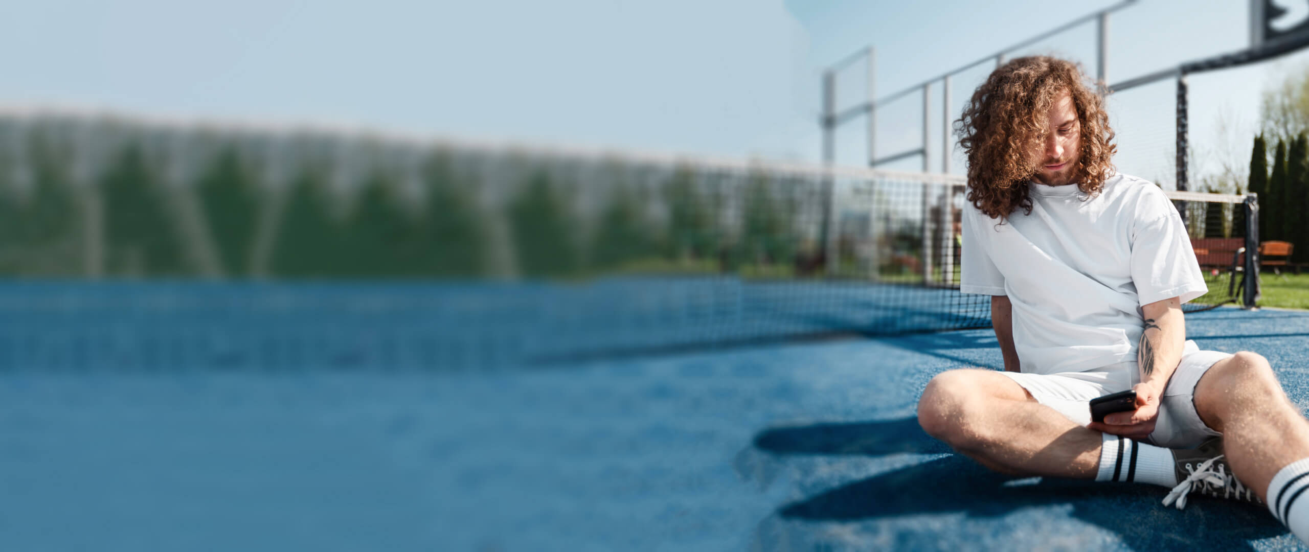 A padel player taking a break on the court while browsing news and updates related to the sport on their mobile device.
